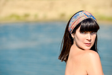 Portrait of a beautiful sexy brunette girl with bare shoulders on the beach in sunny weather