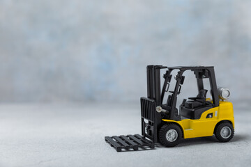Yellow forklift on bright textured background. Logistics concept. Logistics and supply chain management for online shopping concept. Delivery of goods or products to the store worldwide. Cardboard box