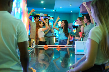 Group of friends having fun playing air hockey and celebrating their victory in an amusement park