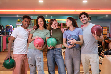 Five friends holding bowling balls, smiling and enjoying their time together at the bowling alley
