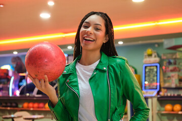 Happy customer holding a red bowling ball, smiling, in a bowling alley