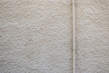 Textured wall with rough plaster finish and vertical plastic pipe. Neutral color, minimalist background