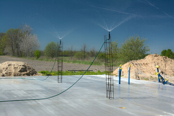 Budowa domu, pielęgnacja świeżej płyty fundamentowej poprzez zraszanie betonu wodą © gpmax