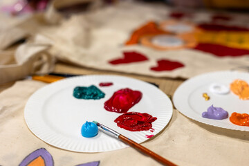 Acrylic paints on paper plates for fabric painting workshop, creative art process with colorful palette and brush.