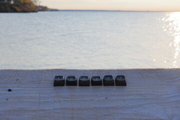 Keyboard letters spelling the word logout on weathered wood with shimmering water at sunset in the background