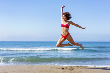 Carefree woman in swimwear jumping on beach