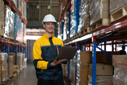 Man warehouse worker wearing uniform and helmet safety standing with clipboard for checking stock products on shelves in warehouse. Logistics, Distribution Center concept