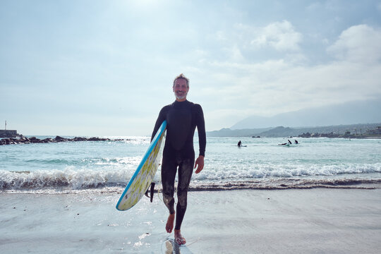 Surfer walking out of the ocean carrying surfboard on sunny day