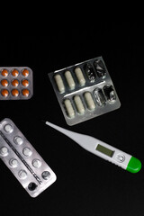 Vertical photo, various pills in blister packs and a thermometer on a black background