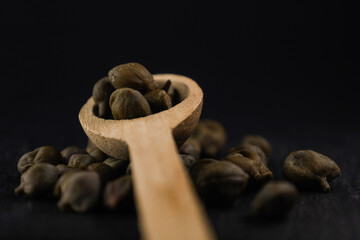 Capperi versati da cucchiaino di legno su nero.