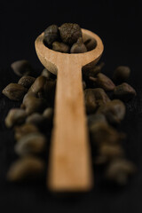 Still life: cucchiaino di legno e capperi su nero.