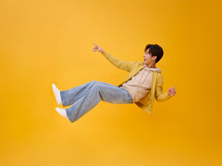 Happy smiling asian man relaxing floating in mid-air and hand pointing finger isolated on yellow...