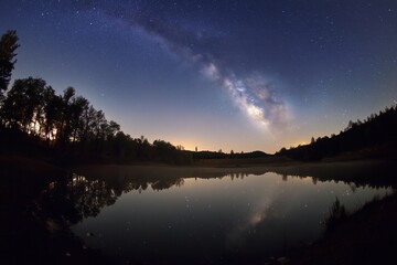 A serene lake mirroring the ethereal milky way galaxy under a starlit night sky.