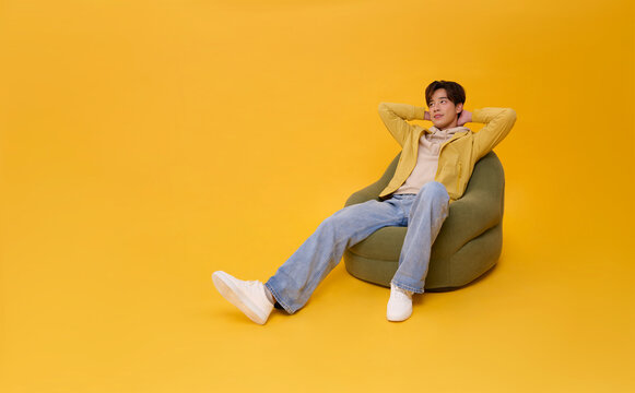 Full body Happy smiling young asian handsome man relaxing sitting on sofa isolated on yellow background. Lifestyle concept
