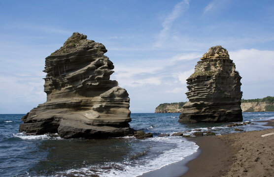 Majestic coastal rock formations rising dramatically from azure waters under a clear blue sky, showcasing nature's artistry and timeless beauty in a serene landscape
