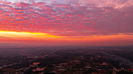 Aerial shot of a gorgeous sunrise. A panoramic view of dramatic mountain peaks silhouetted against a vibrant sunset sky, with fiery hues of red, orange, and pink blending into the fading blue.