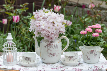 romantisches Arrangement mit Blumenstrauß aus japanischen Säulenkirsch-Blüten (Prunus serrulata), Gänseblümchen (Bellis perennis) und vintage Porzellan