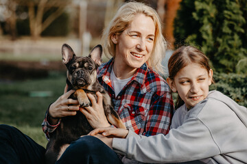 Joyful woman and daughter sitting on lawn in summer with bulldog puppy
