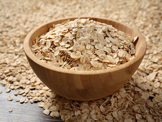 Oat grains in a wooden bowl and scattered on the table.