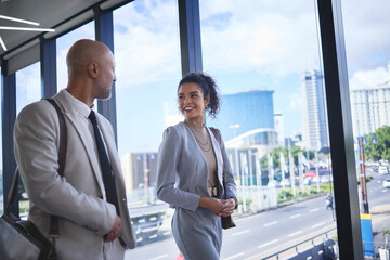 Fototapeta premium Collaboration, smile and walking with corporate people in airport together for international travel. Business, conversation or teamwork with man and woman employee on bridge in terminal for flight