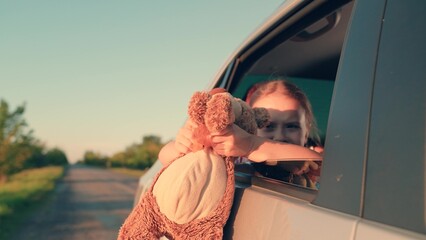 little girl with toy bear. happy face child daughter from window with teddy bear. happy family. mother daughter traveling car. happy mother child back seat car going trip. face childish smile.