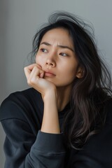 A woman with long hair is sitting with her hands on her knees. She has a sad expression on her face