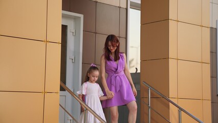 little schoolgirl holds mother hand while going down stairs school. happy family. lifestyle mother...