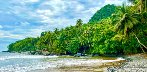 Lush tropical forest and palm-covered hills meet the rocky coastline of São Tomé and Príncipe. A...