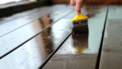 Close-up of a brush painting wood floor in brown color. Wood plank impregnation. Finish oil coating of board. Second layer of oiling. Manual construction work in a gazebo. Natural building materials.