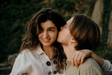 Obraz premium Close-up of a man kissing a smiling woman on the forehead, showing affection and tenderness in a countryside setting. Woman and man in love on date in park.