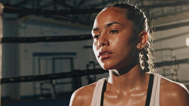 Athletic young female boxer resting between rounds, determined face glistening with sweat