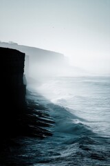 Sunlit Coastal Cliff View with Crashing Waves and Atmospheric Haze for Timeless Scene