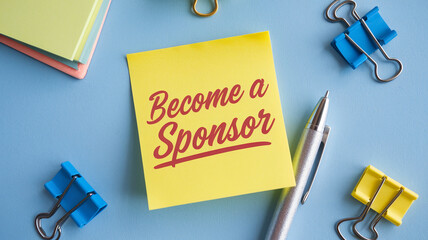 Yellow sticky note with "Become a Sponsor" text, surrounded by stationery on blue background, showcasing sponsorship opportunity, ideal for business or fundraising