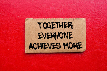 Together everyone achieves more message written on ripped torn cardboard paper piece on red background. Conceptual together everyone achieves more symbol. Copy space.