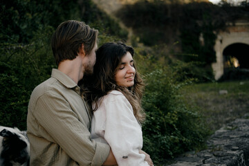 Close-up portrait of a young smiling couple embracing outdoors, surrounded by lush greenery. Natural and authentic love story moment. Woman and man in love on date in park.
