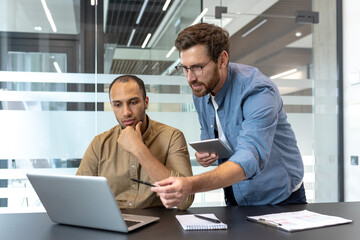 Two colleagues collaborate in a modern office setting, discussing information displayed on a laptop screen with focus and intent.