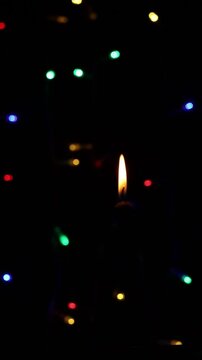 Una toma de cerca de una vela blanca con llama rodeada de varias luces con bombillos de varios colores en movimiento en la oscuridad.