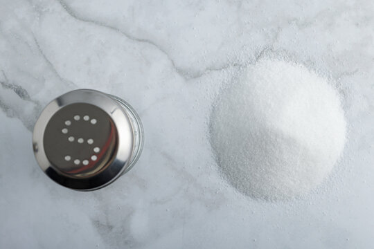 Heap of fine salt and salt shaker and a h on marble countertop