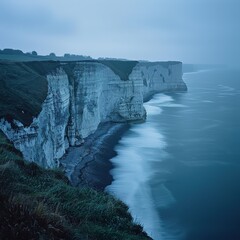 A cool-toned coastal cliff at sunrise, with cool shades of blue and green illuminating the landscape, the ocean below stretching into the distance.