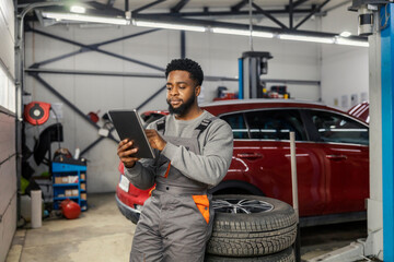 Portrait of african american auto mechanic scrolling on tablet at mechanic workshop.
