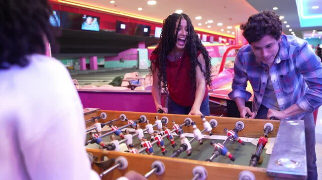 Young adults enjoying a foosball game at the bowling alley, celebrating their victory with a warm embrace