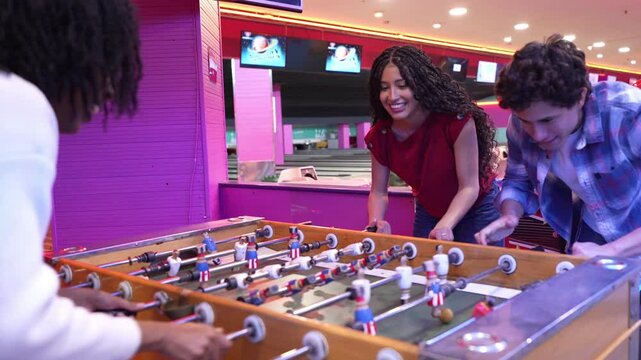 Young adults enjoying a friendly game of foosball in slow motion, adding excitement to their bowling alley outing