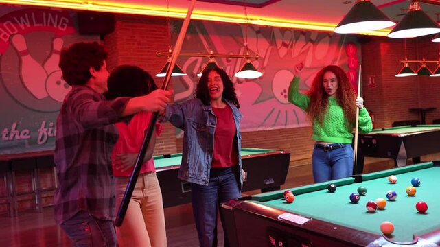 Young friends cheering wildly after scoring winning pool shot, celebrating victory with energetic slow motion excitement in dimly lit bowling alley or bar setting