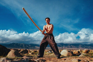Emotional screaming strong man with fighting stick training in high mountains