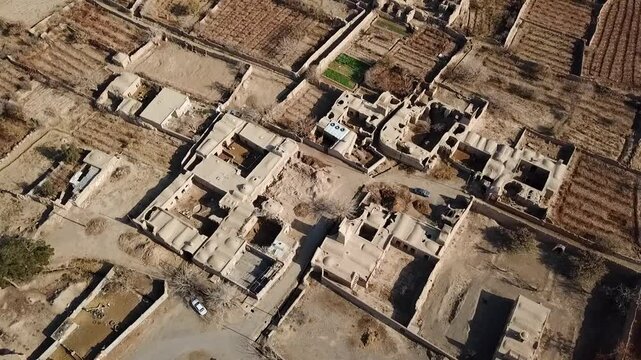 Aerial drone shot rural desert village mosque clay rooftops houses brown dry land middle east traditional Islamic town Iran environment architecture ancient region sunlit settlement buildings earth