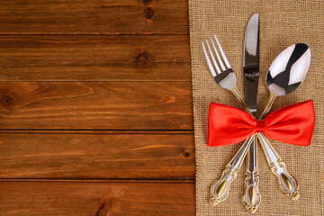 Elegant silverware tied with a red bow on burlap fabric over a rustic wooden table, creating a festive and sophisticated setting perfect for holiday meals, weddings, or celebration visuals.