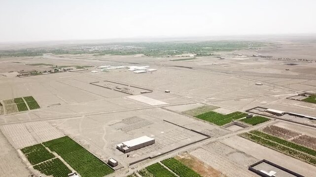 High aerial drone view of a desert plain with large-scale grid-like agricultural plots, scattered buildings, and minimal vegetation. This semi-arid farmland illustrates extensive irrigation planning