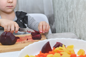 cute girl cuts beetroot for salad with a knife.