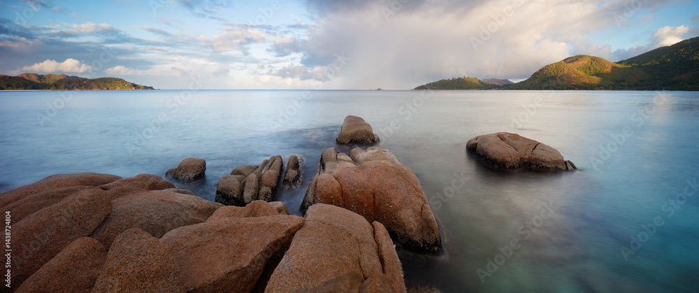 Poster a rocky shoreline with a calm ocean in the background. the sky is cloudy and the water is a deep blu