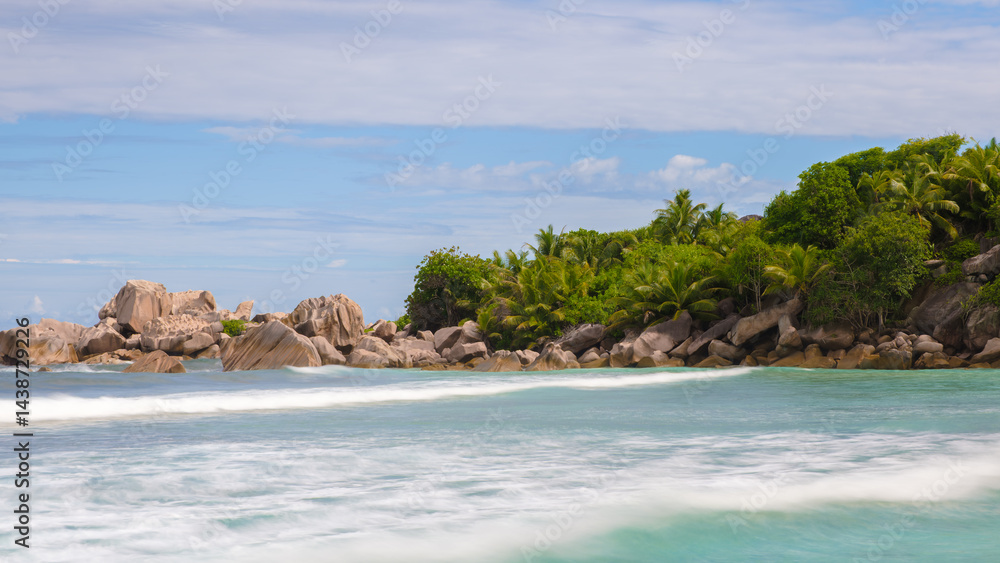 Poster a beautiful beach with a rocky shoreline and a clear blue sky. the water is calm and the waves are s